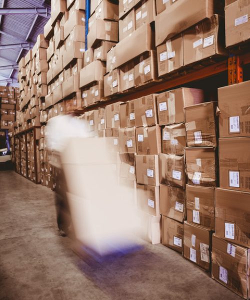 Blurred worker with fork pallet truck stacker with boxes in warehouse