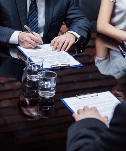 Hands of the businessmen sitting on the meeting and signing the contract.